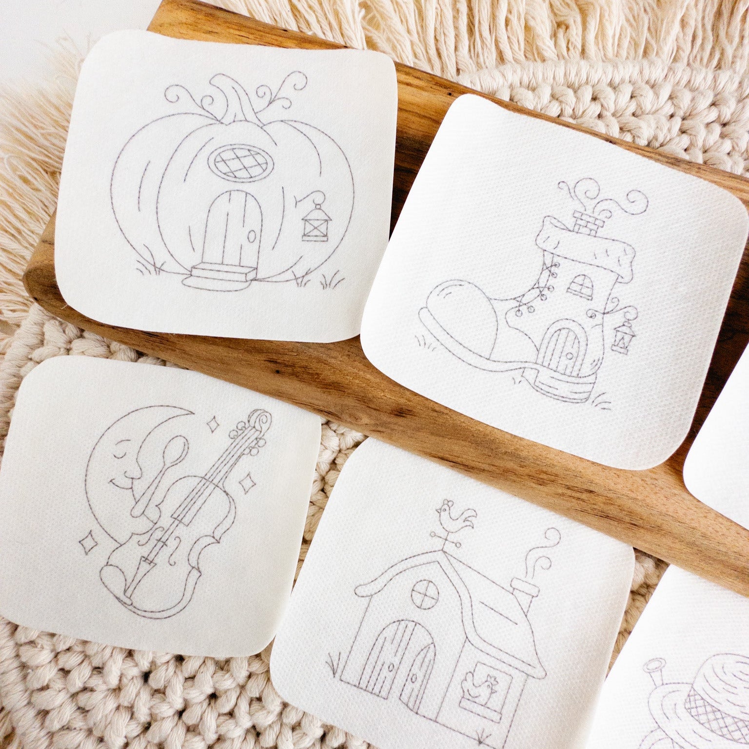 Six white water-soluble stick and stitch embroidery patterns featuring nursery rhyme designs like a pumpkin house and a boot house.