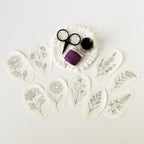 Nine oval, water-soluble prairie flower embroidery patterns with black outlines, purple thread, scissors, and pins.