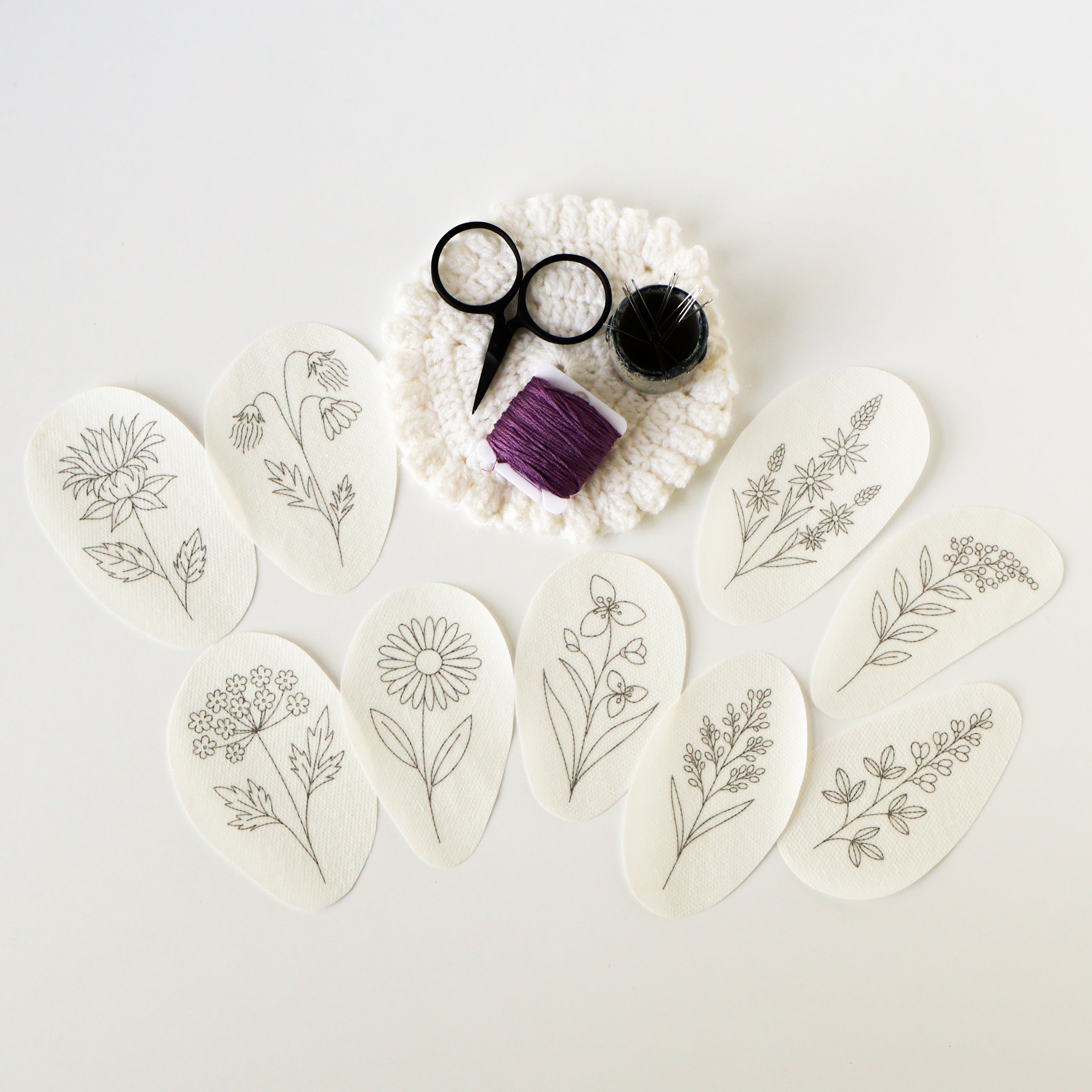 Nine oval, water-soluble prairie flower embroidery patterns with black outlines, purple thread, scissors, and pins.