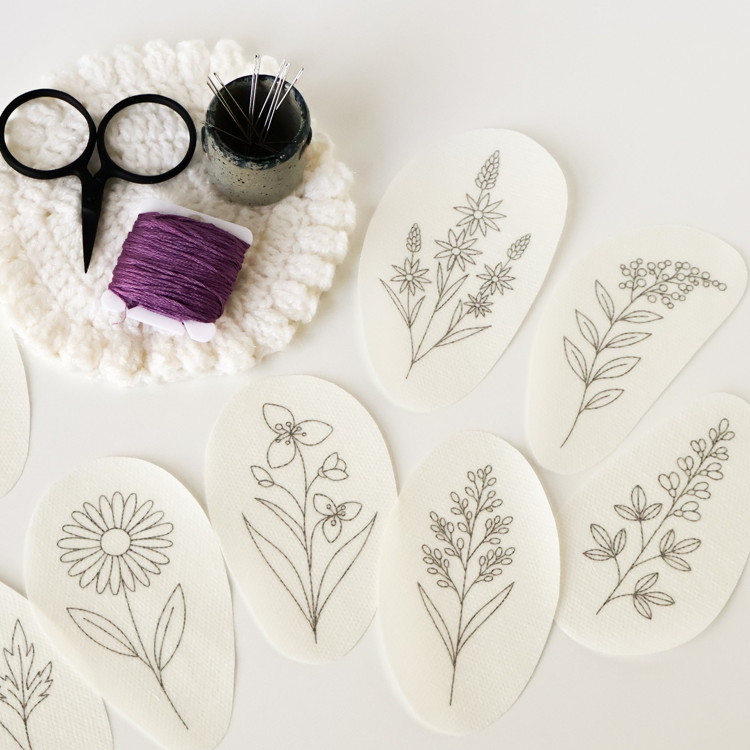 Nine oval water-soluble embroidery patterns with outline prairie flower designs, purple thread, scissors, and pins.