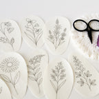 Nine oval, white water-soluble embroidery patterns with black prairie flower designs, thread, and scissors.