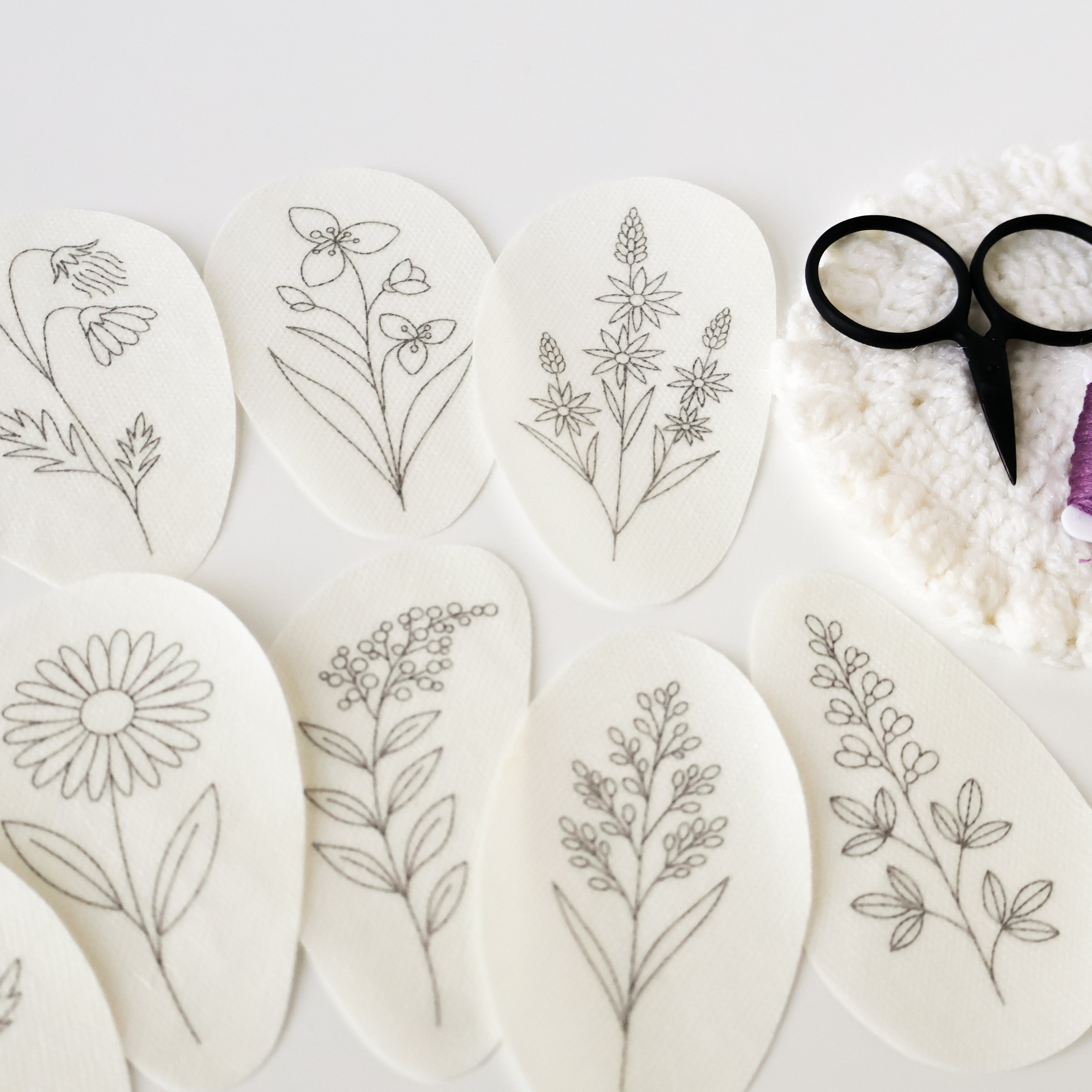 Nine oval, white water-soluble embroidery patterns with black prairie flower designs, thread, and scissors.