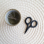 Ceramic bowl with embroidery needles and black scissors on a textured white surface