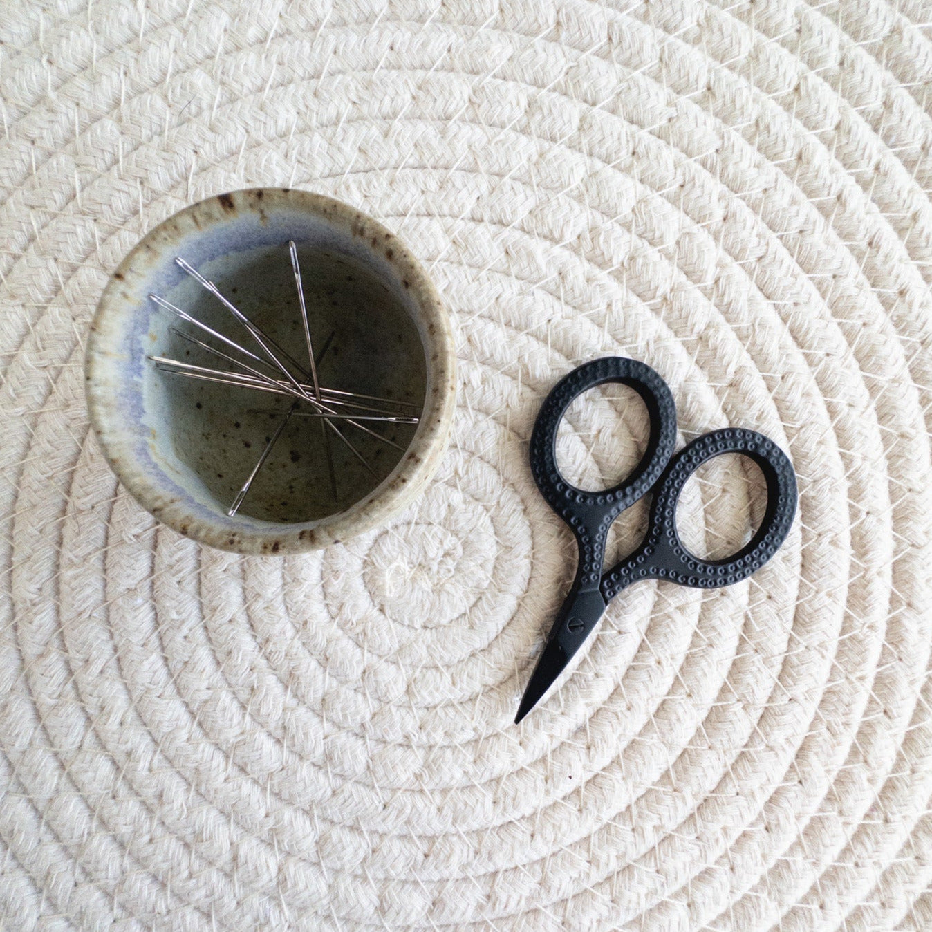 Ceramic bowl with embroidery needles and black scissors on a textured white surface