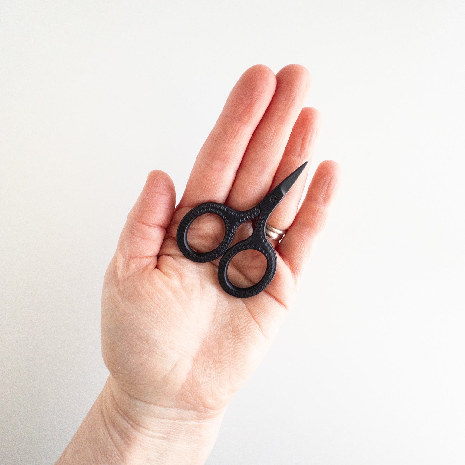 Hand holding a small pair of black scissors against a white background