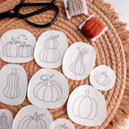 13 pumpkin stick and stitch embroidery patterns on white water-soluble stabilizer, with scissors and floss.