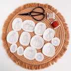 13 pumpkin stick and stitch embroidery patterns on white water-soluble stabilizer, with scissors and floss.