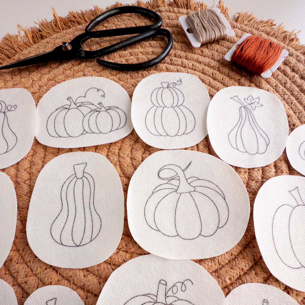 White water-soluble stabilizer patches with black outline pumpkin embroidery patterns, scissors, and embroidery floss.