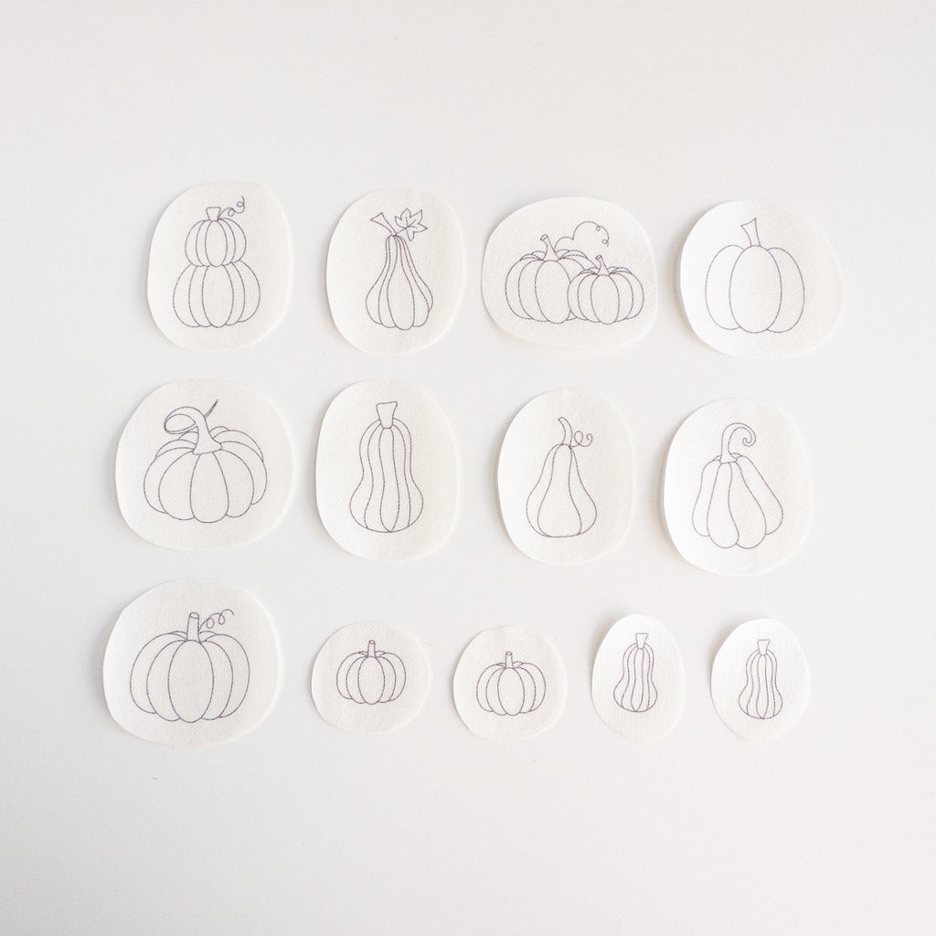 Thirteen white water-soluble stabilizer patches with various gray pumpkin embroidery patterns.