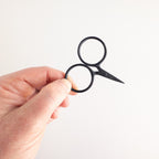 Hand holding a small pair of black scissors against a light gray background