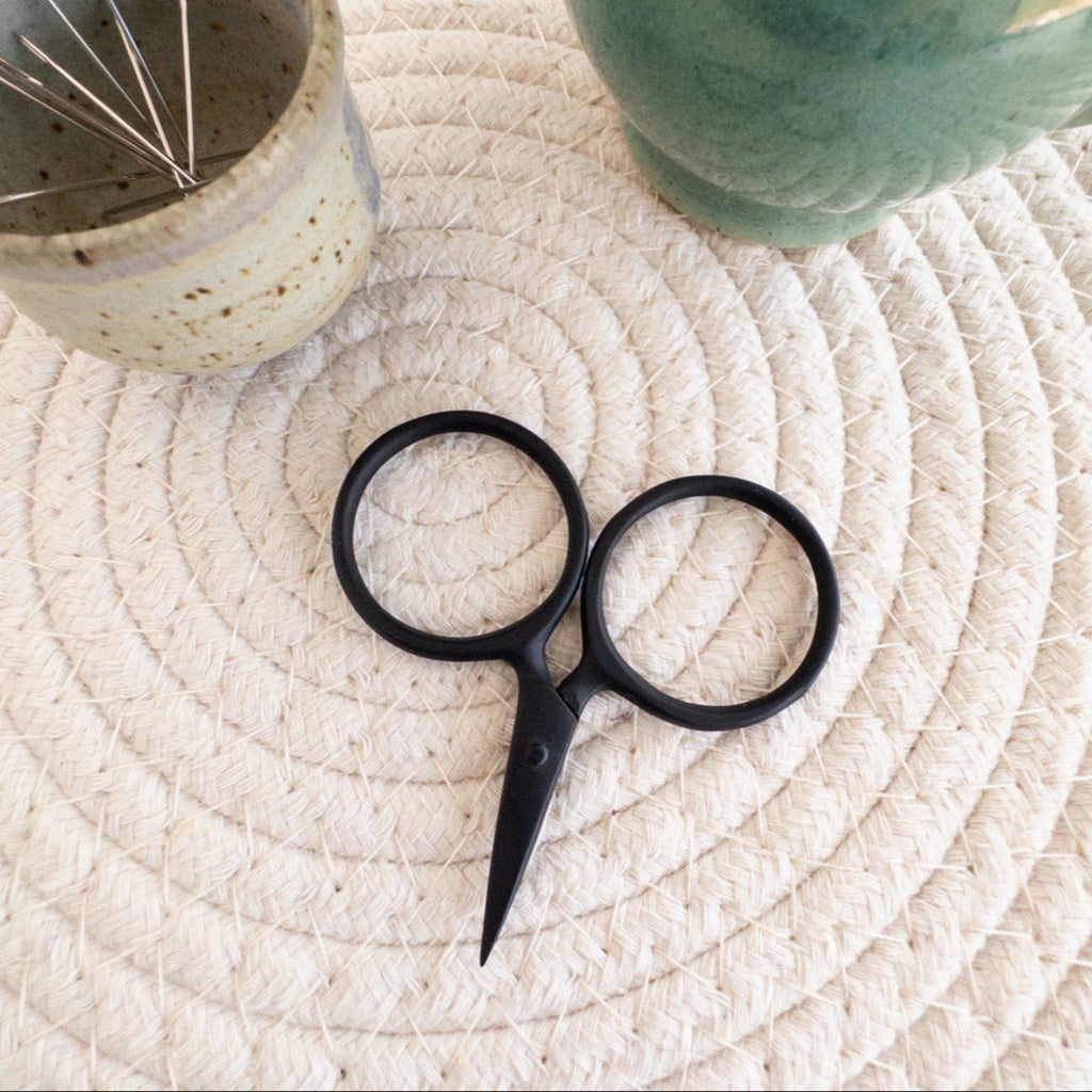 Black scissors, ceramic container with pins, and green ceramic pitcher on a textured surface