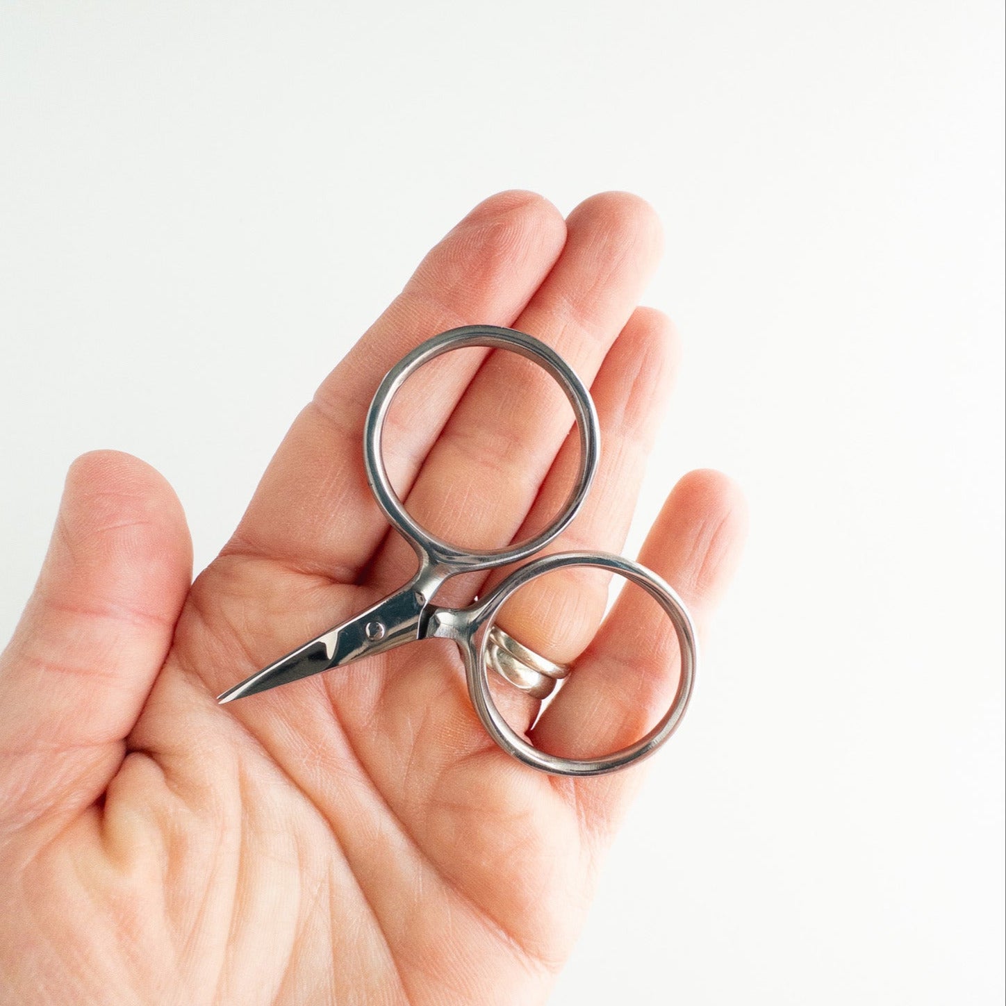 Hand holding a small pair of silver scissors against a light background