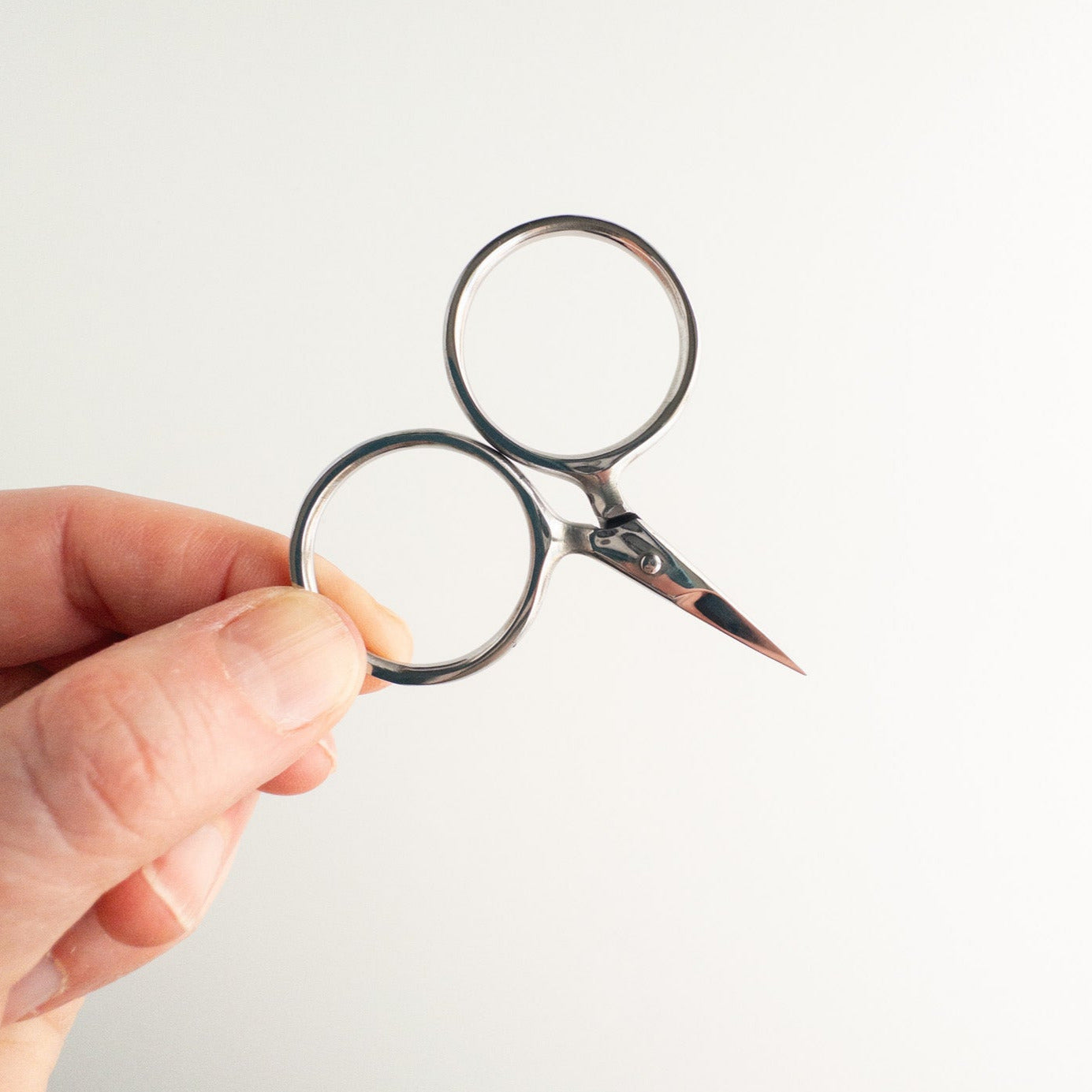 Hand holding a pair of small scissors against a white background