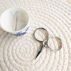 Scissors and a small cup with needles on a textured white surface