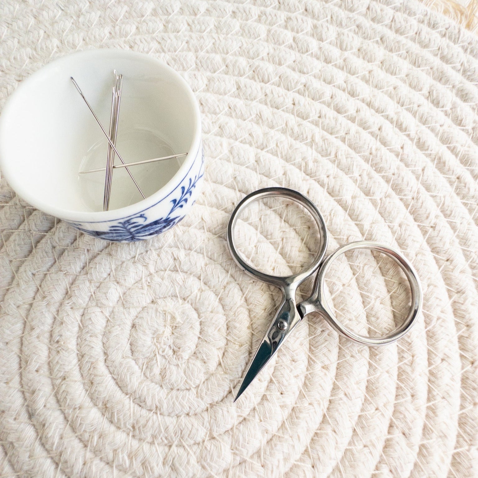 Scissors and a small cup with needles on a textured white surface