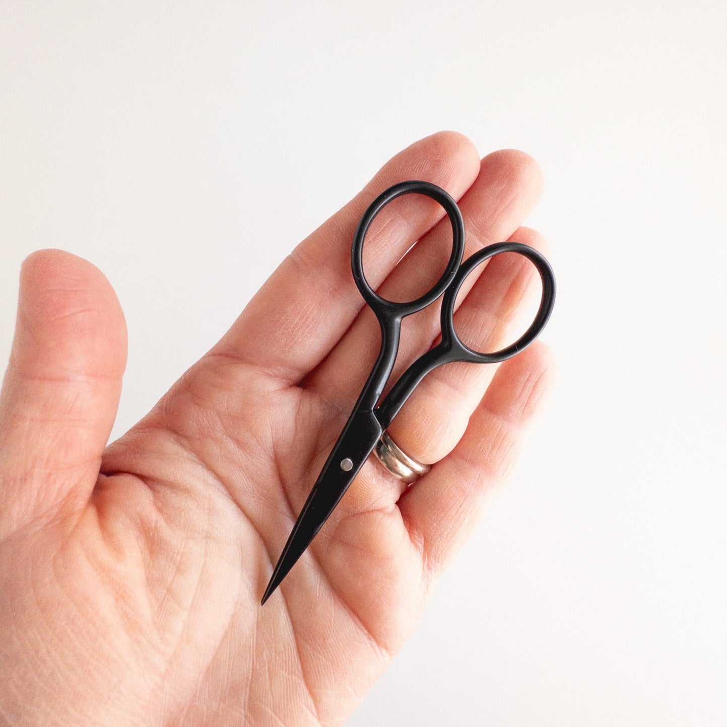 Hand holding a small pair of black scissors against a white background
