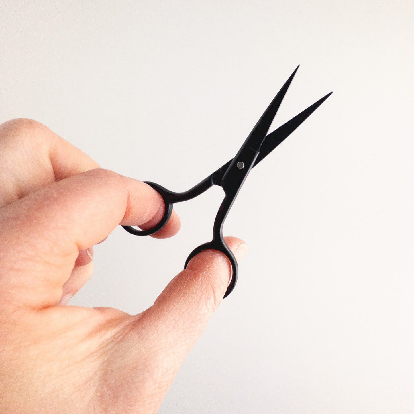 Hand holding a pair of black scissors against a light gray background