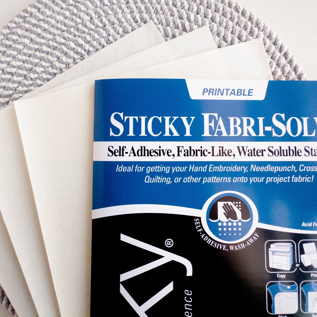 Sulky Printable Sticky Fabri-Solvy paper sheets on a textured gray and white background.