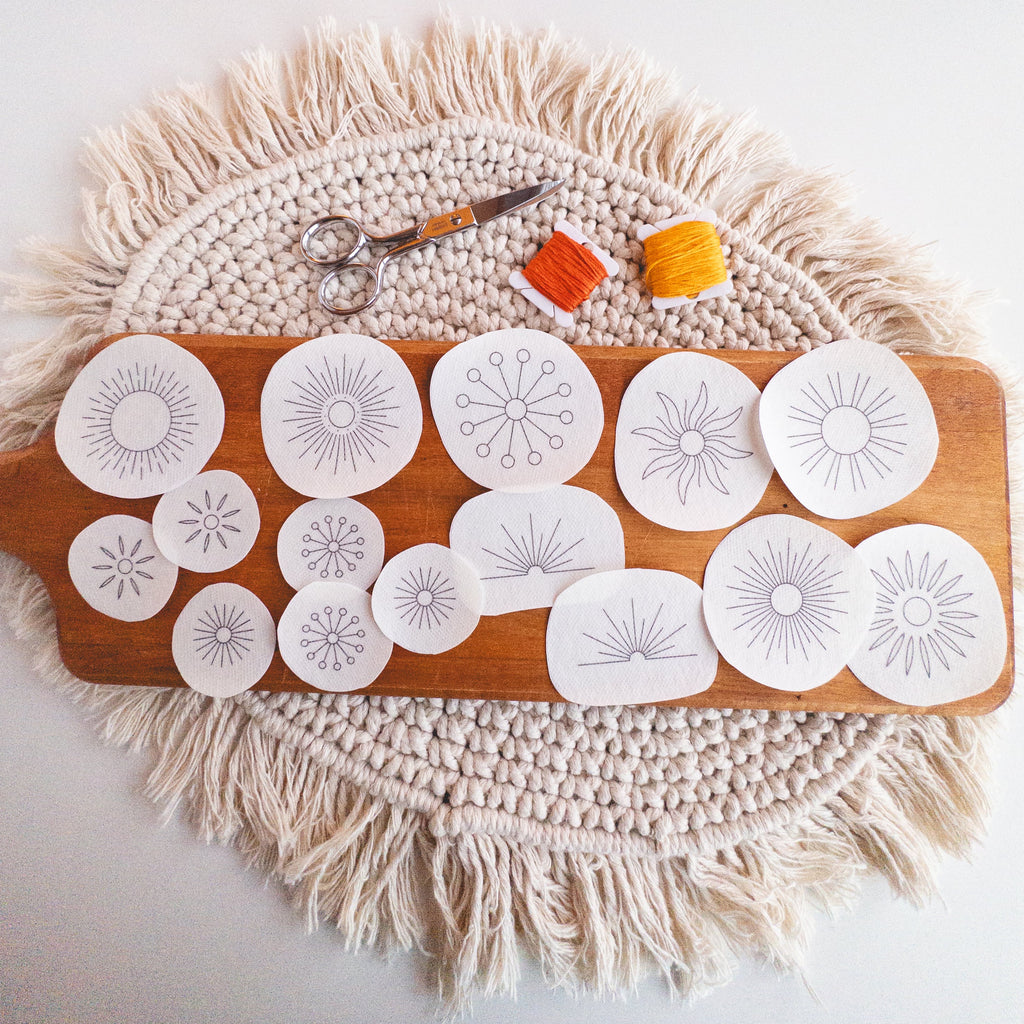 Sunburst Stick and Stitch embroidery patterns on water-soluble stabilizer, with scissors and orange/yellow floss.