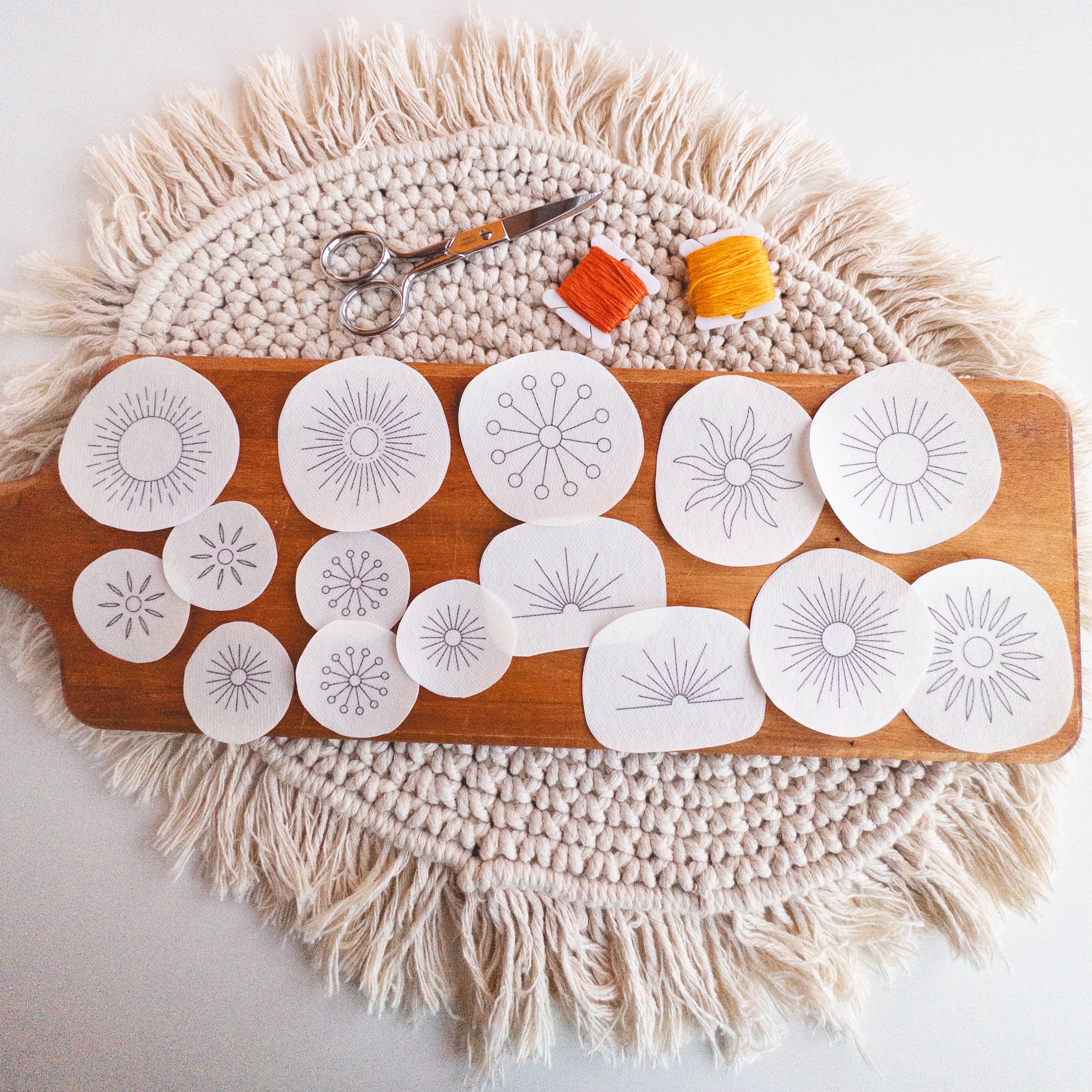 Sunburst Stick and Stitch embroidery patterns on water-soluble stabilizer, with scissors and orange/yellow floss.