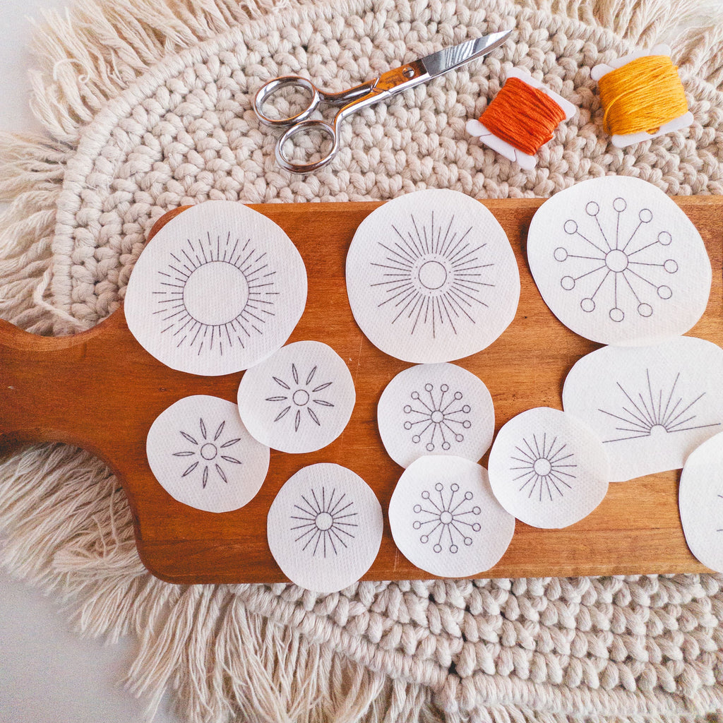 Sunburst Stick and Stitch embroidery patterns on a wooden board with scissors and orange/yellow floss.