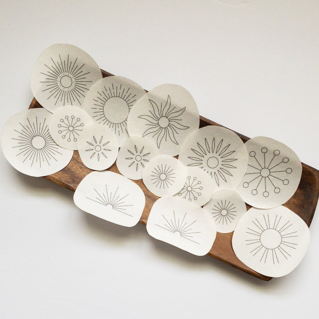 15 white water-soluble sunburst embroidery patterns on a wooden tray, varying in size and design.