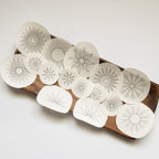 15 white water-soluble sunburst embroidery patterns on a wooden tray, varying in size and design.