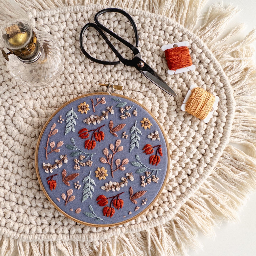 Twilight Meadow embroidery pattern in a 6-inch hoop, featuring fall wildflowers on moody blue fabric with thread and scissors.