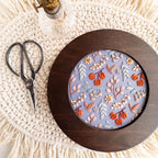 Twilight Meadow embroidery in a dark wood 6-inch hoop, featuring fall florals on moody fabric, with scissors and lamp.