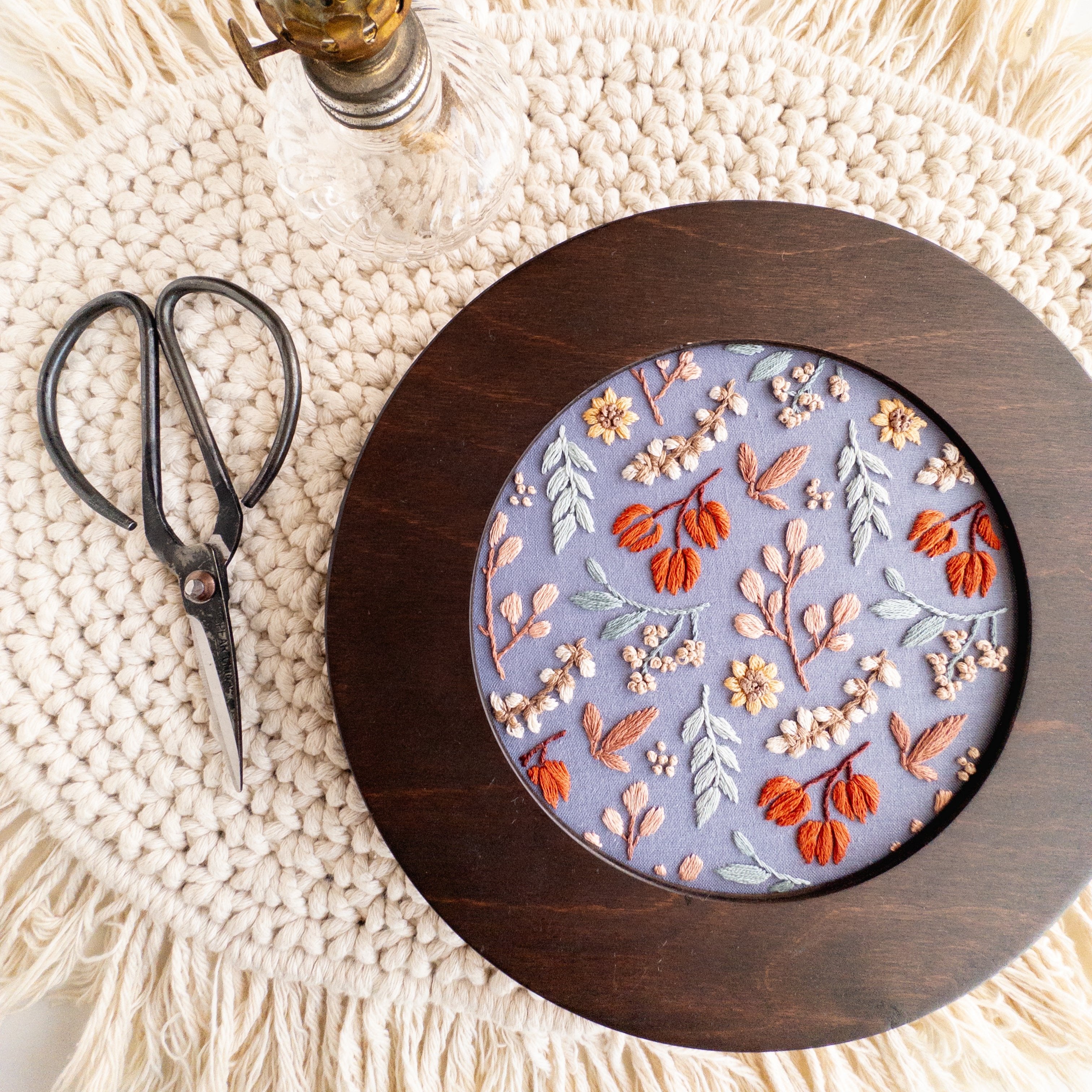 Twilight Meadow embroidery in a dark wood 6-inch hoop, featuring fall florals on moody fabric, with scissors and lamp.