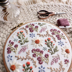 Embroidered wildflower field with daisies, lavender, and small flowers in a 6-inch hoop on a textured background.