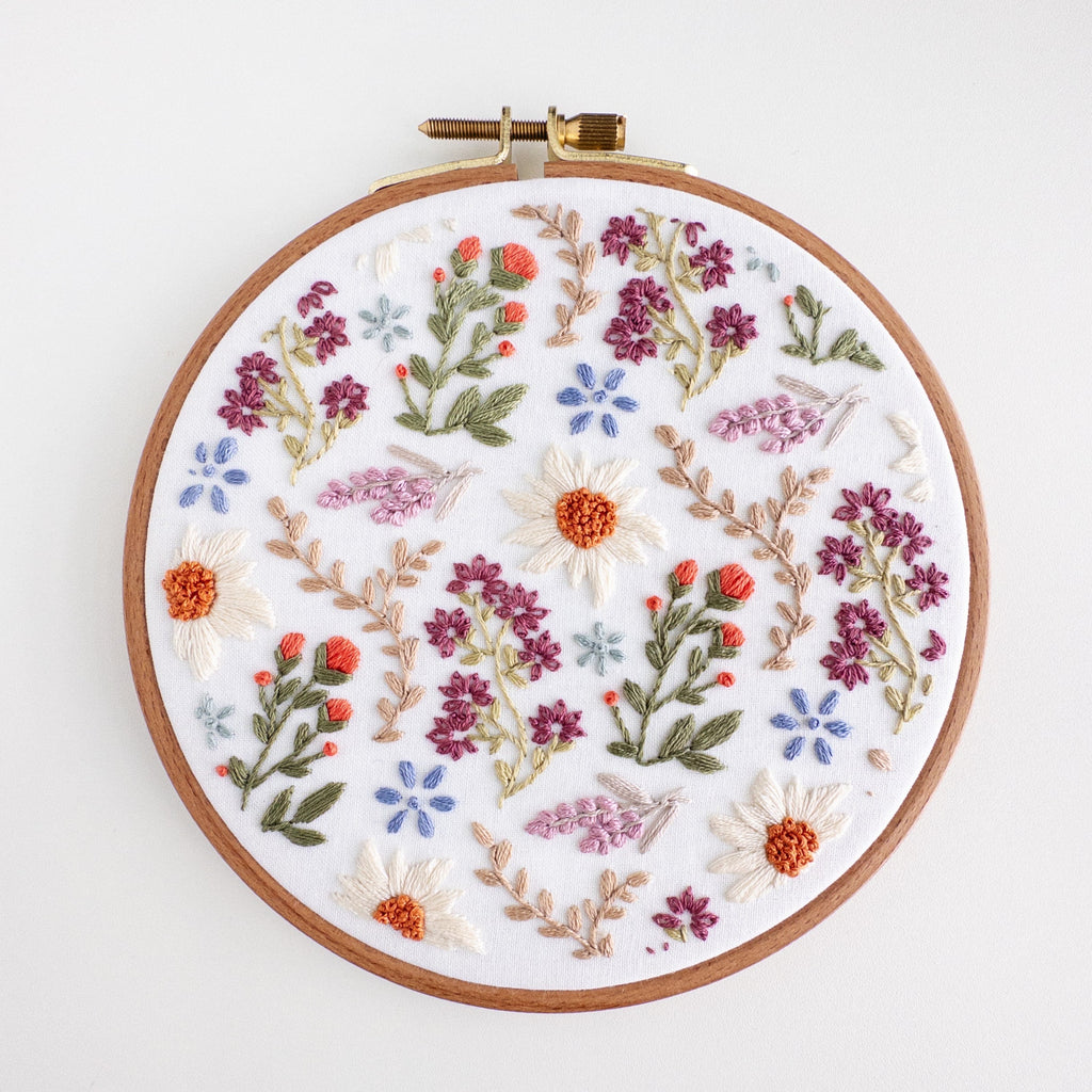 A 6-inch embroidery hoop with a white fabric featuring a colorful wildflower field pattern.