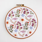 A 6-inch embroidery hoop with a white fabric featuring a colorful wildflower field pattern.