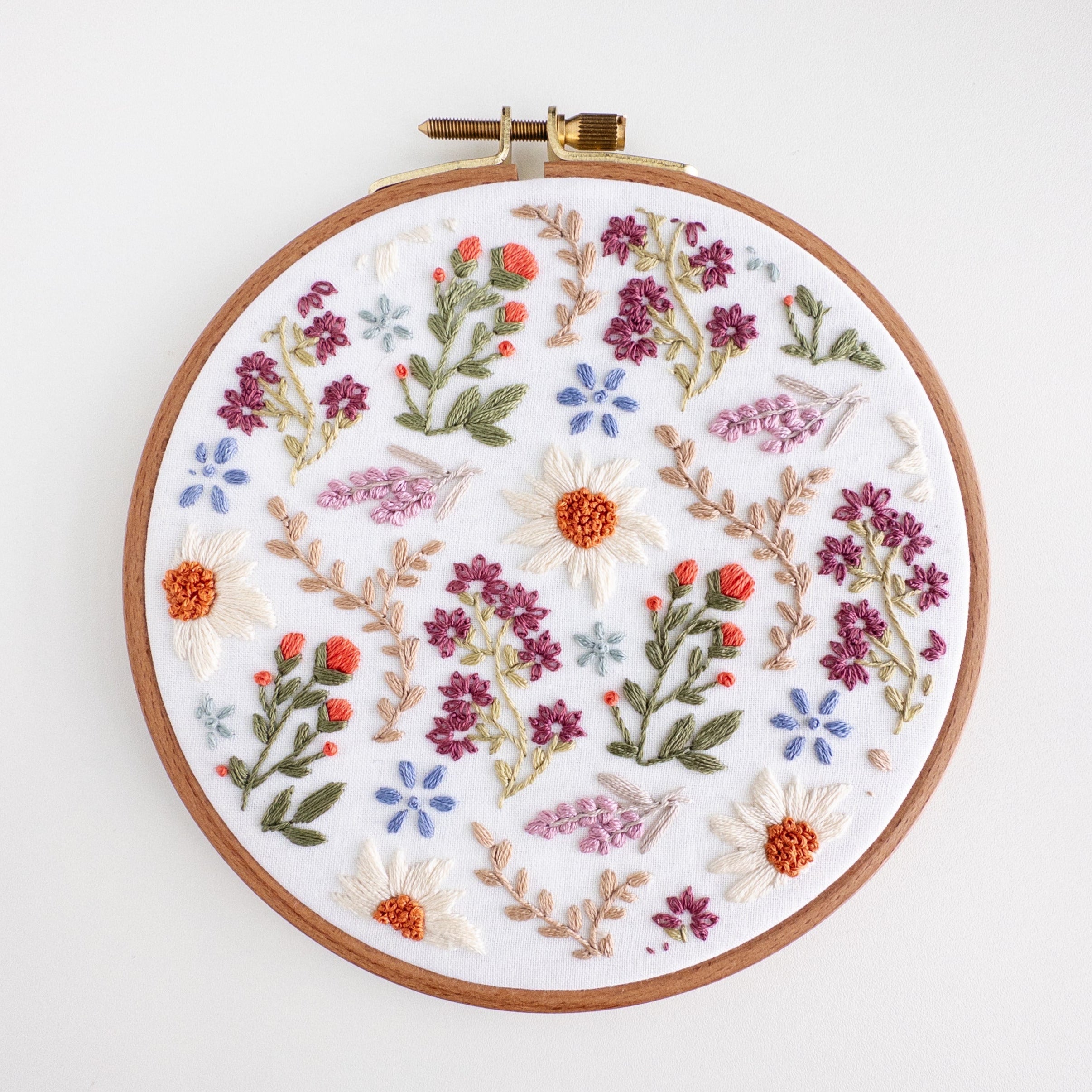 A 6-inch embroidery hoop with a white fabric featuring a colorful wildflower field pattern.