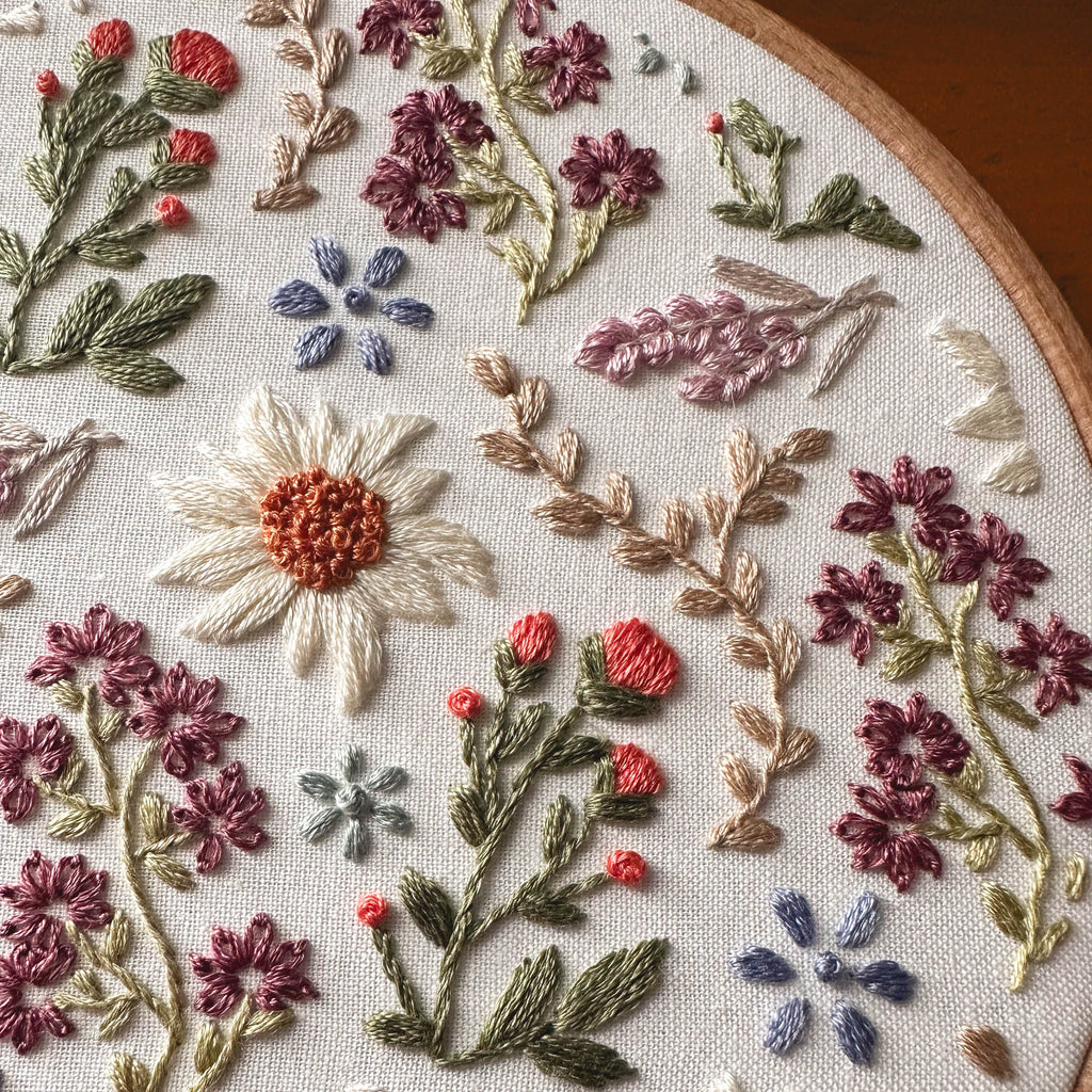 Close-up of a wildflower embroidery pattern with colorful daisies, lavender, and floral designs on white fabric in a hoop.
