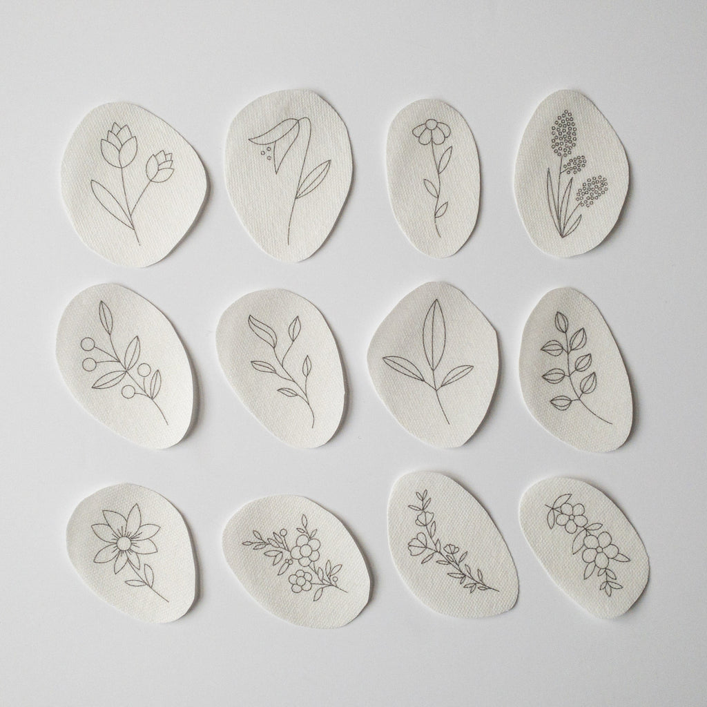 Twelve oval, water-soluble stick and stitch patches with various black line art wildflower embroidery patterns.