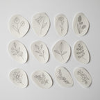 Twelve oval, water-soluble stick and stitch patches with various black line art wildflower embroidery patterns.
