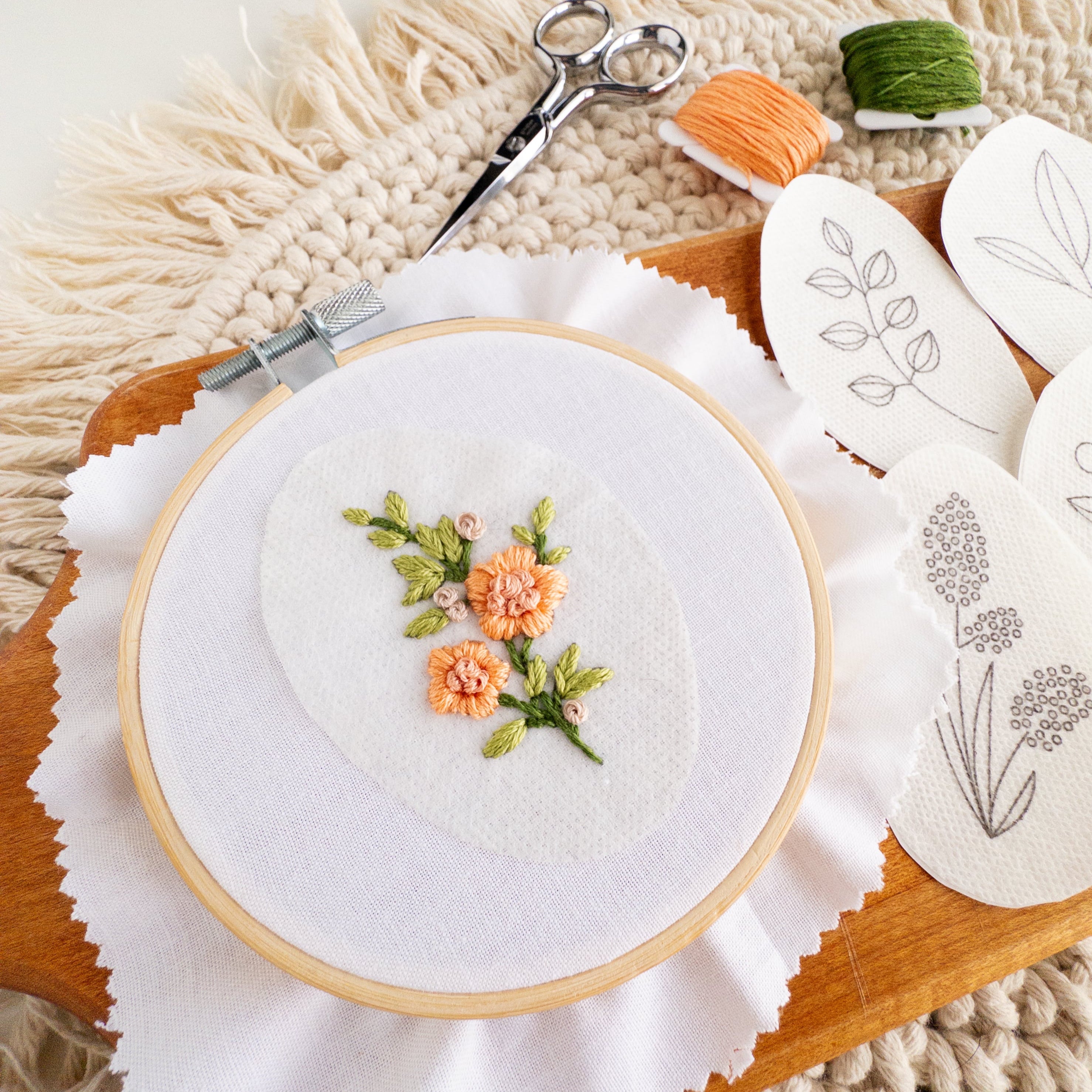 Embroidered peach wildflowers on a stick and stitch patch in a hoop, with other patterns and floss.